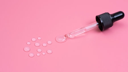 Pipette with transparent liquid, drops on a pink background.の写真素材