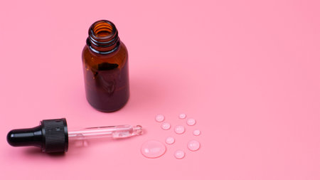 Dark glass container with transparent liquid and a pipette on a pink backgroundの写真素材