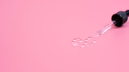 Drops of transparent gel are squeezed out of a pipette on a pink background. copy spaceの写真素材