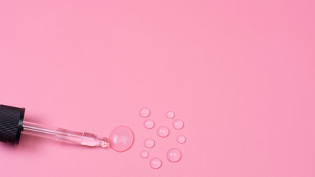 Drops of transparent gel are squeezed out of a pipette on a pink backgroundの写真素材