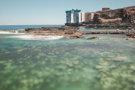 A beautiful scenery of transparent sea under the sunset sky surrounded by buildingsの写真素材