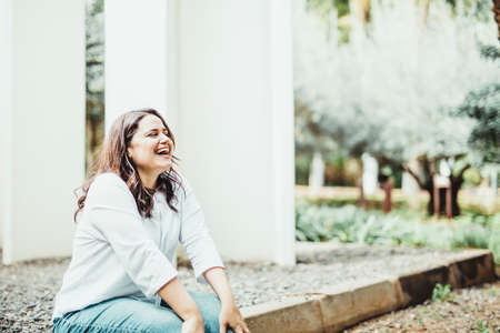 laughing woman sitting on the ground in a park with a backdrop of white columns