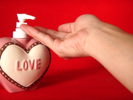 action of hand receiving the hand cleanser gel from the heart shape of bottle with letter  Love   on it and red background           の写真素材