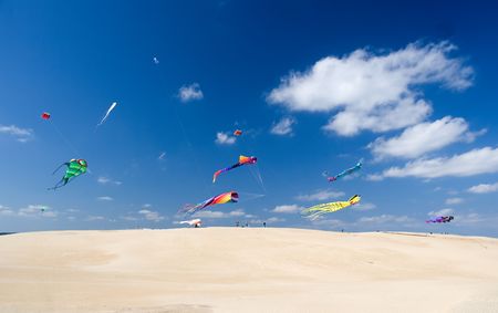Multicolor kites flying over sandy hill in bright sunny afternoonの写真素材