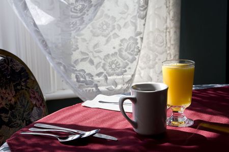Glass of orange juice and cap of coffee on a table chair highlighted by the sunlight from  the window.の写真素材