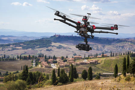 A flying helicopter with raised landing gears and a camera with blured hills of Tuscany in the backgroundの写真素材