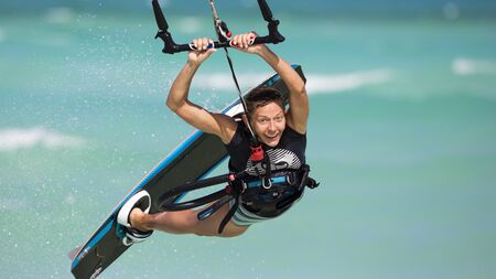 A smiling girl performing a relay jump on a kiteboard. The subject is surrounded with drops of water and tropical sea in the background.の写真素材