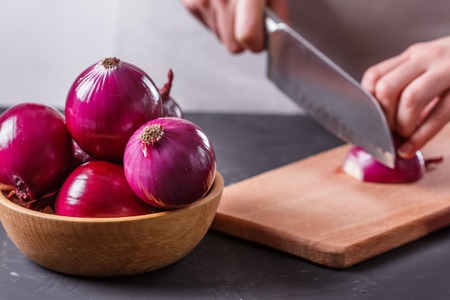 young woman in a gray aprons cuts red onion.の写真素材