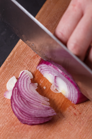 young woman in a gray aprons cuts red onion.の写真素材
