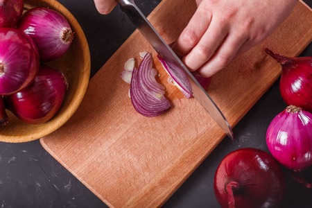 young woman in a gray aprons cuts red onion.