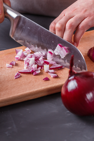 young woman in a gray aprons cuts red onion.の写真素材