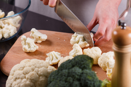 young woman in a gray aprons cuts cauliflower broccoli.の写真素材