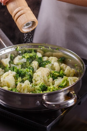 young woman in a gray apron roasts cauliflower broccoli.の写真素材