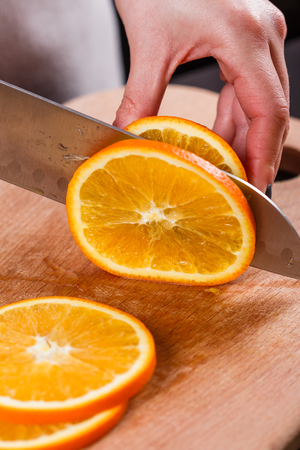 young woman in a gray aprons cuts an orange.の写真素材