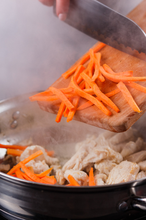 young woman in a gray aprons roasts chicken fillet with carrots.の写真素材