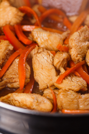 young woman in a gray aprons roasts chicken fillet with carrots.の写真素材