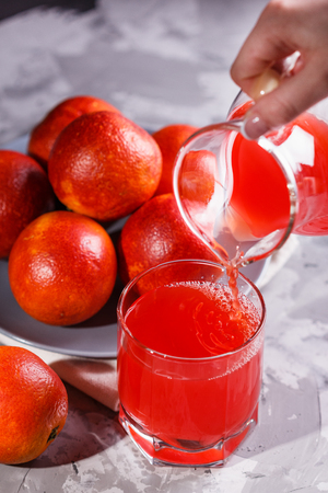 young woman in a gray apron pours juice blood orange.の写真素材