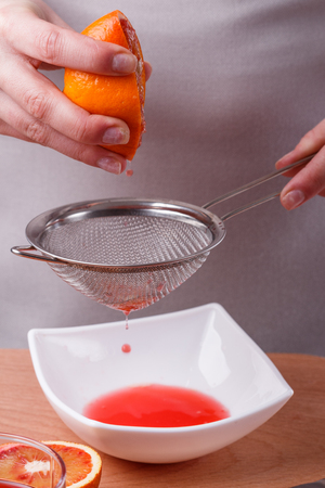 young woman in a gray apron squeezes juice of orange blood.の写真素材