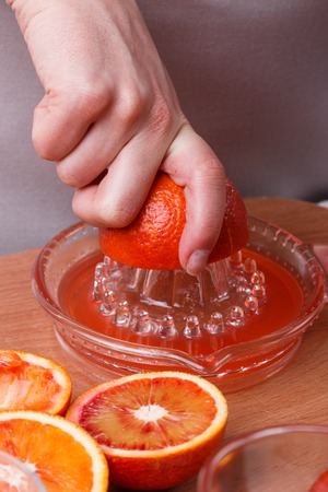 young woman in a gray apron squeezes juice of orange blood.の写真素材