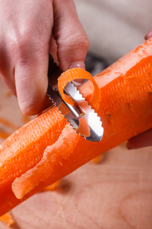 young woman in gray apron peeling carrots.の写真素材