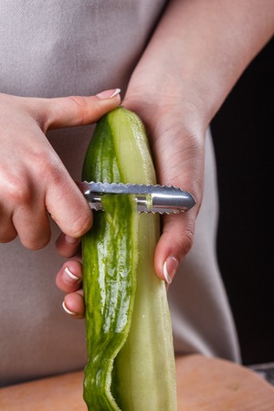young woman in gray apron peeling cucumber.の写真素材