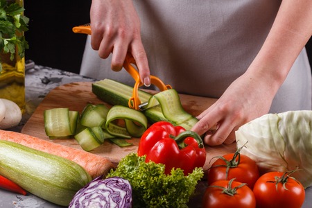 young woman in a gray apron cuts a cucumber.の写真素材