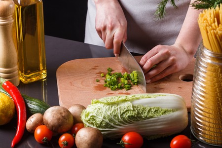 young woman slicing herbs in a gray apron.