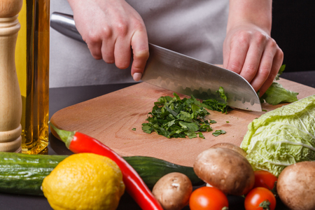 young woman slicing herbs in a gray apron.の写真素材