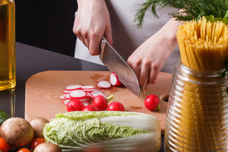 young woman in a gray apron cuts a radish.の写真素材