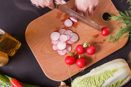 young woman in a gray apron cuts a radish.の写真素材