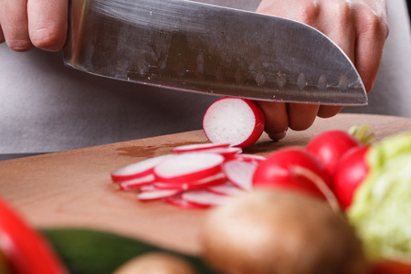 young woman in a gray apron cuts a radish.の写真素材
