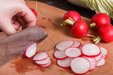 young woman in a gray apron cuts a radish.の写真素材