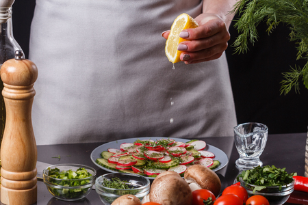 young woman in a gray apron is preparing a cucumber and radish salad.の写真素材