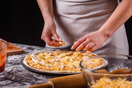 young woman in a gray aprons prepares a Hawaiian pizza.の写真素材