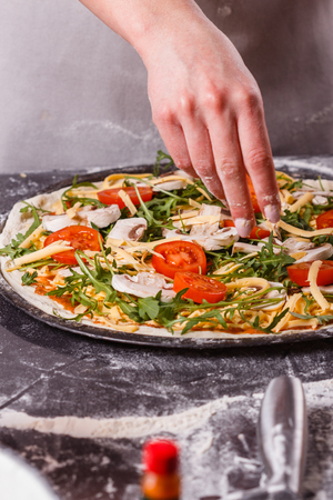 young woman in a gray aprong prepares a vegetarian pizza.の写真素材