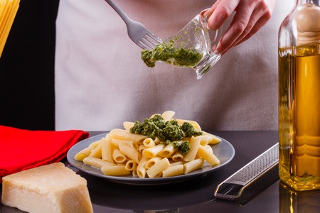 young woman in a gray apron is preparing pasta pesto.