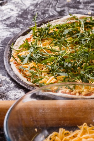 young woman in a gray aprong prepares a vegetarian pizza.の写真素材