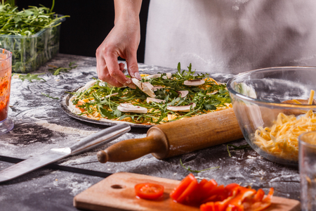 young woman in a gray aprong prepares a vegetarian pizza.の写真素材