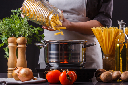 young woman in a gray apron preparing pasta.の写真素材