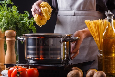 young woman in a gray apron preparing pasta.の写真素材