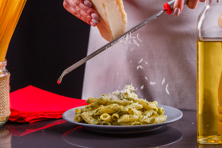 young woman in a gray apron is preparing pasta pesto.の写真素材