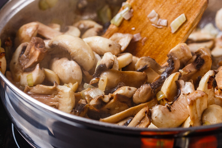 young woman in a gray apron roasts mushrooms in a frying pan.の写真素材