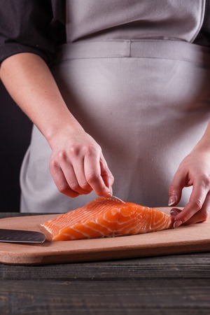 young woman removes bones from a salmon fillet.の写真素材