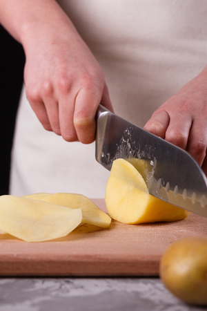 young woman in an apron cuts potatoes.の写真素材