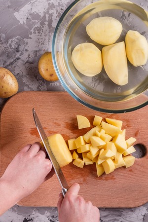 young woman in an apron cuts potatoes.の写真素材