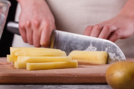 young woman in an apron cuts potatoes.の写真素材