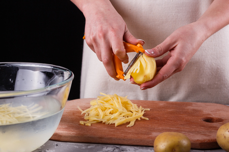 young woman in an apron cuts potatoes.の写真素材