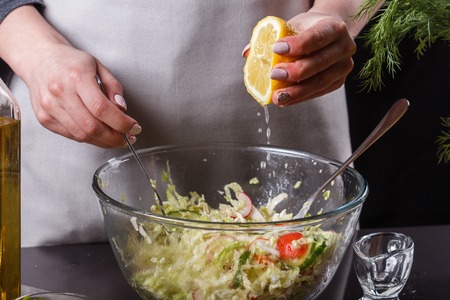 A young woman in a gray apron adds lemon juice to a cabbage salad.