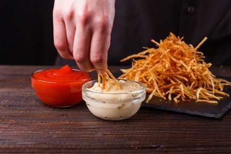young woman dip fried potatoes to mayonnaise sauce.の写真素材