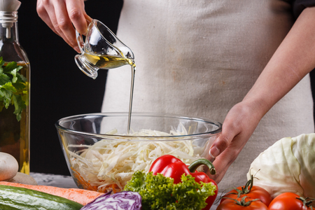 a young woman in a gray apron adds a vinegar to a cabbage salad.の写真素材